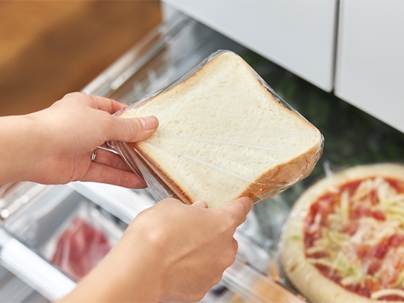 冷凍庫から取り出したラップに包まれた食パンを手に持っている様子
