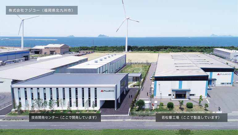 福岡県北九州市にある株式会社フジコーの本社・若松工場と技術開発センター。風車が立ち並ぶ海沿いに位置し、光触媒技術の研究・製造が行われている様子。