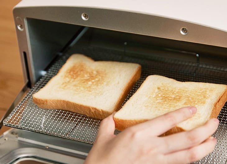 アラジントースターの焼き網の上に食パン2枚が並び、片方はこんがりきつね色に焼けている様子