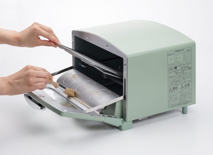 アラジントースターでこんがり焼けた食パンをトングで取り出している様子、グリーン色のレトロなデザインが特徴的なトースター